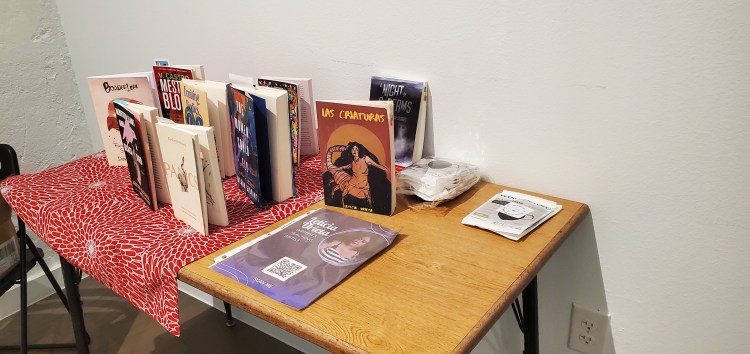 A collection of books standing up on a table with a purple flyer and a set of masks. 