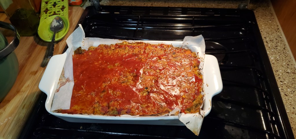 A vegan meatloaf in a white casserole dish cooling on a black RV propane oven. 