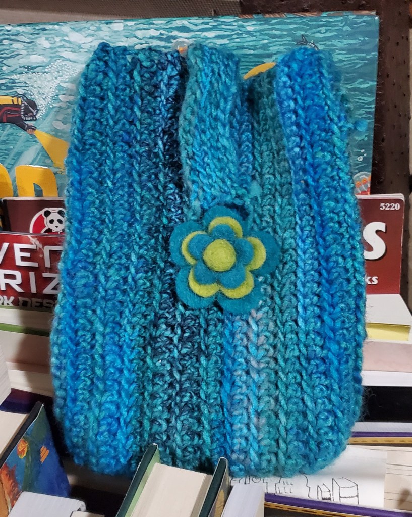 A blue ombre crocheted e-reader case with a blue and green felt flower sown onto it. 