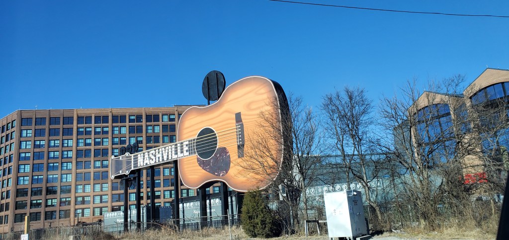 A large acoustic guitar statue that says Nashville on the neck in the middle of a downtown area.