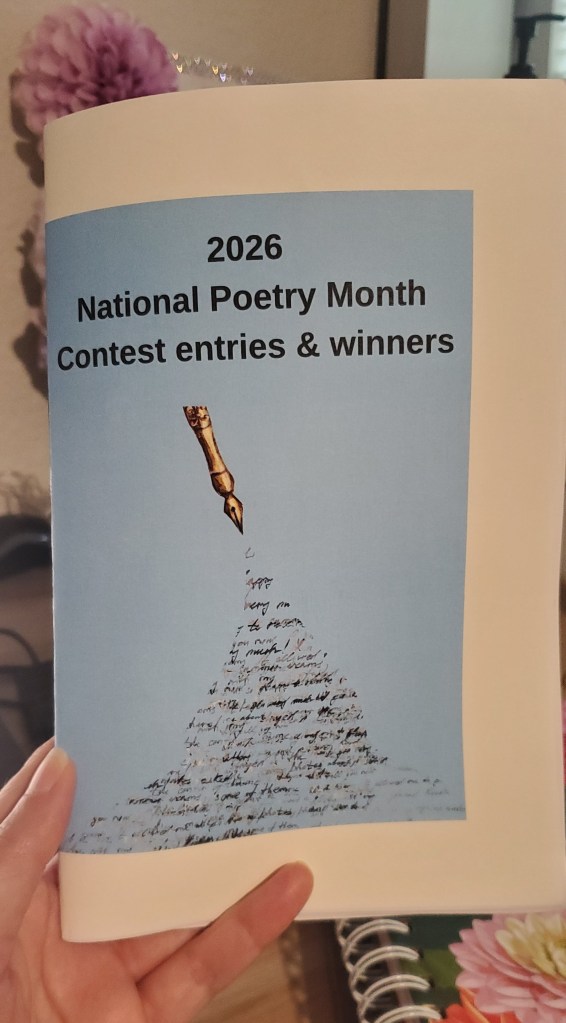 Leticia's hand holding up the Pflugerville Poetry Society 2026 National Poetry Month Contest Entires and Winners chapbook with a sky blue cover with a gold ink pen spilling cursive writing onto the page. 