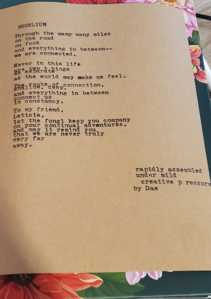 A typewriter poem in black ink on brown paper. The poems says, Mycelium. Through the many miles on the road on foot and everything in between-we are connected. Never in this life are two things separate as the world may make us feel. The roots of connection, shallow, deep, and everything in between, connect us in constancy. To my friend, Leticia, let the fungi keep you company on your continued adventures, and may it remind you that we are never truly very far away.