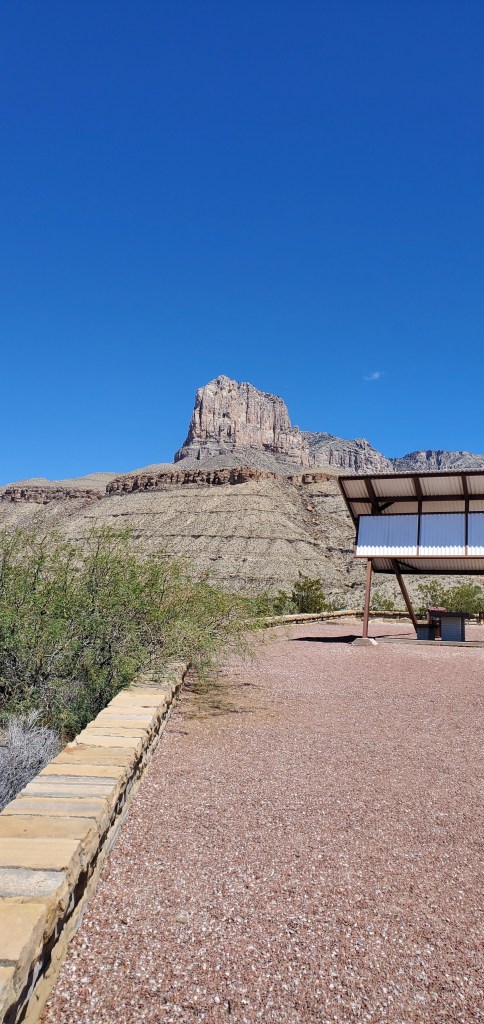 A looming limestone mountain cliff peak under a cloudless blue sky taken from a red stone rest area.