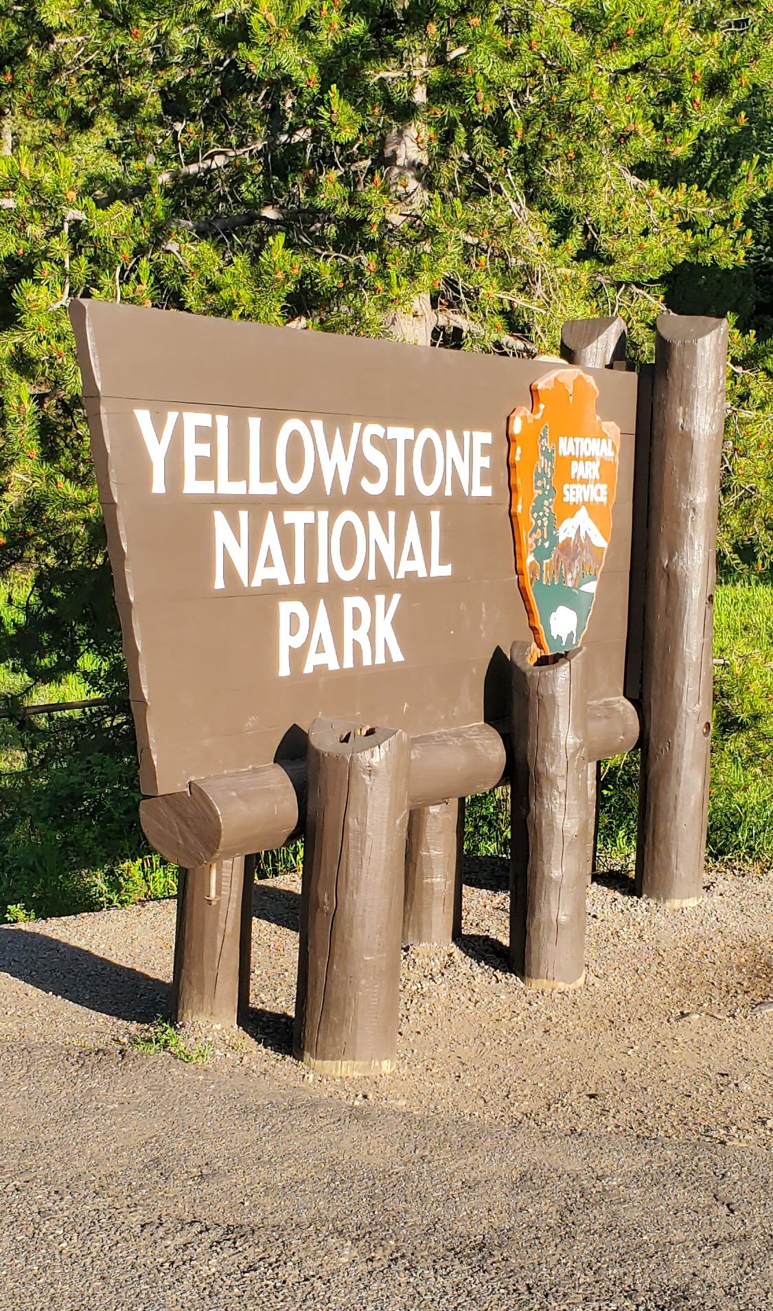 The brown wooden Yellowstone National Park sign with white ink in the soil and the orange National Park Service badge.