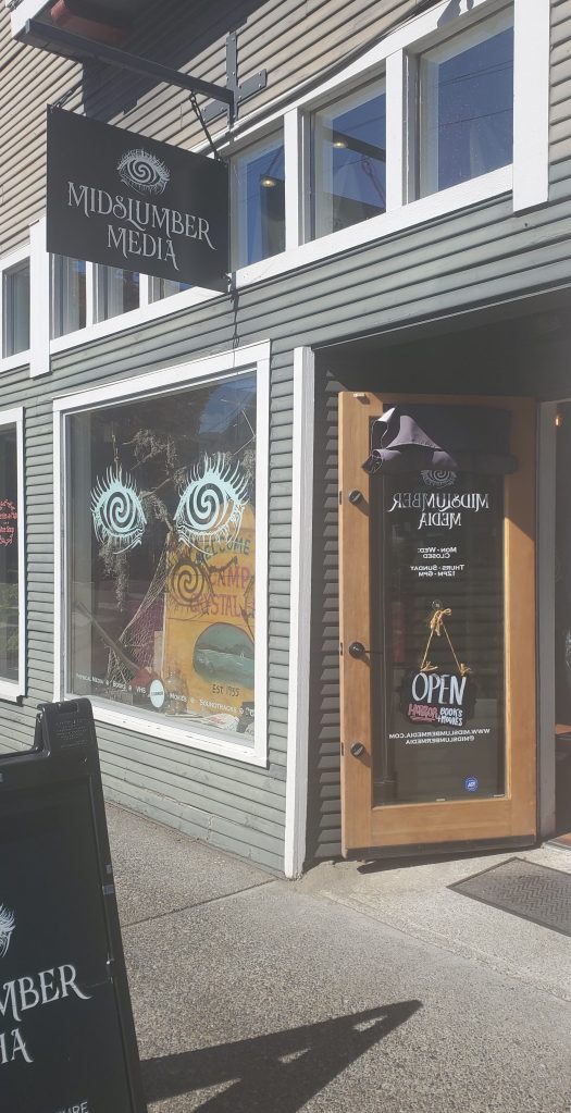 The outside of Midslumber Media, a horror bookstore in Portland, Oregon with their door open and swirling eyes painted on the outside window.