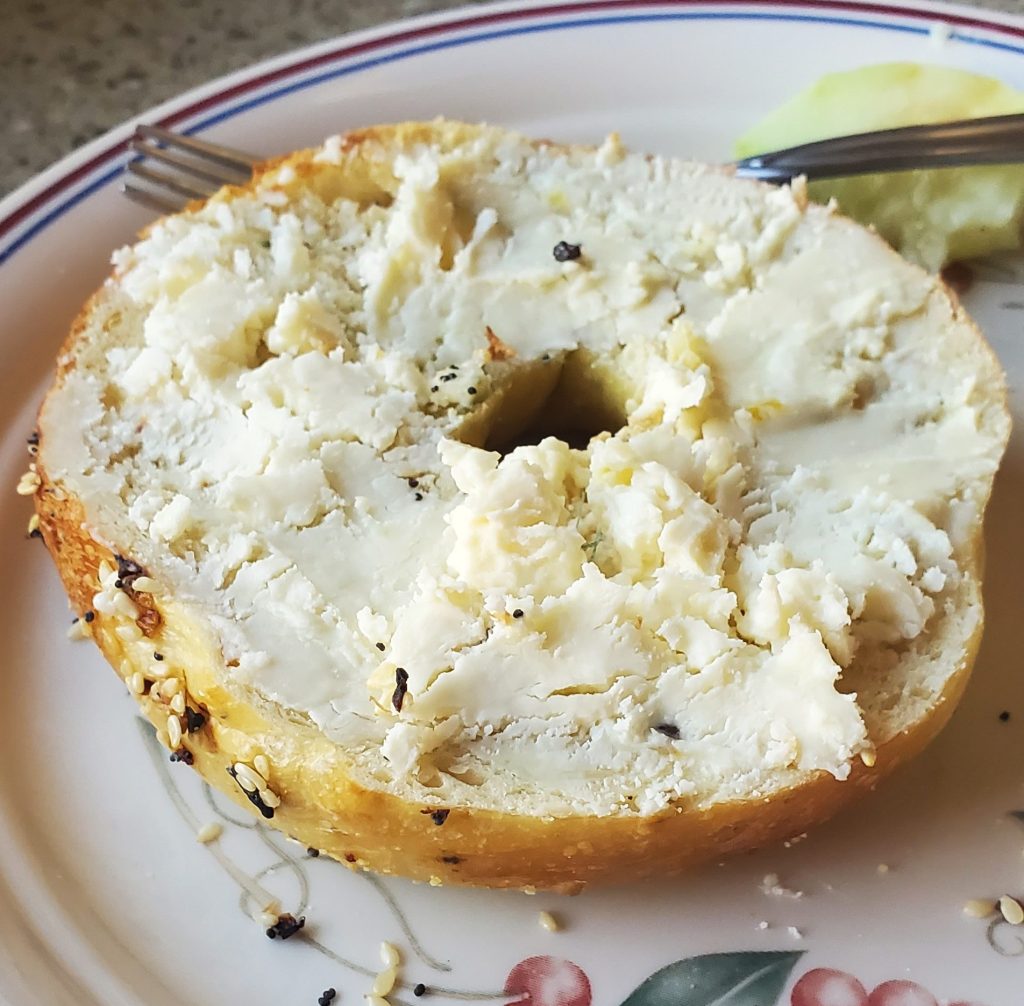 An everything bagel on a ceramic plate covered in blue cheese.