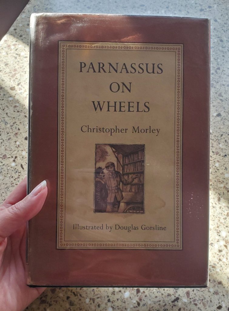 An rare edition of Parnassus on Wheels by Christopher Morley with reddish brown border and an illustration of a white man in a cap selling books from a cart.