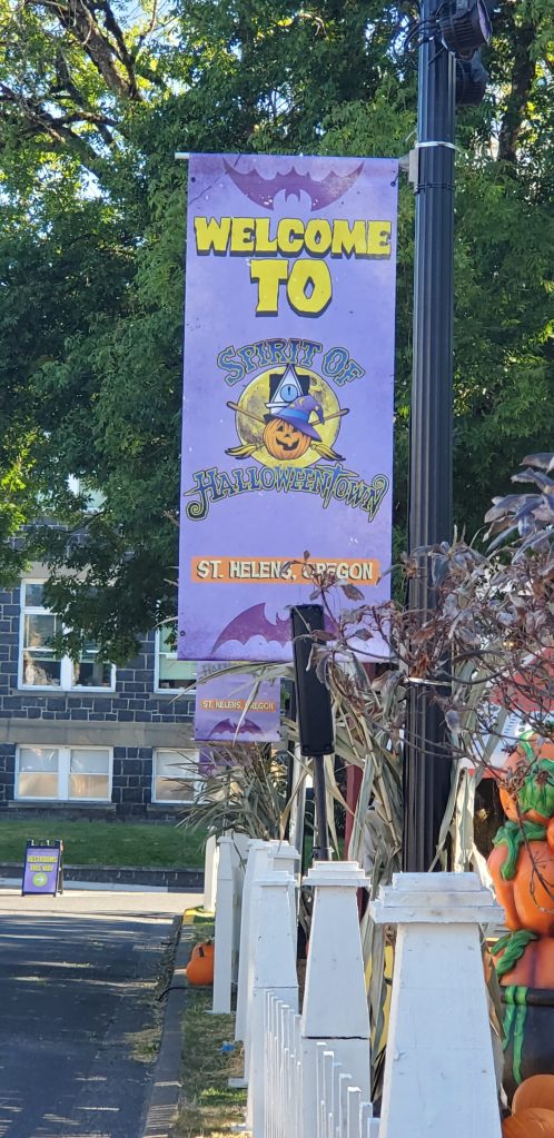 A Purple sign on a black lamppost that says Welcome you Spirit of Halloweentown St. Helens Oregon.